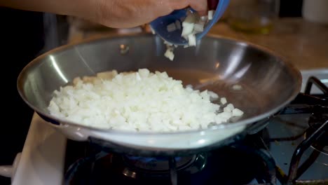 Dumping-dices-onions-in-a-heated-and-oiled-skillet-on-the-stove-top---slow-motion