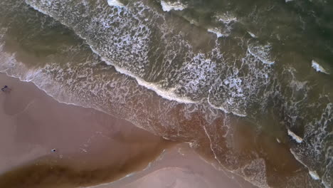 Waves-breaking-on-shore-of-seaside-village-Karwia-in-Poland,-top-down-aerial