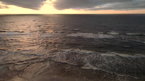 Aerial-shot-of-beautiful-sunset-over-crashing-ocean-waves-on-sandy-beach