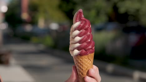 Hand-holding-a-colorful-soft-ice-cream-cone-and-twisting-it-on-itself-on-a-nice-summer-day