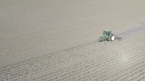 Tractor-ploughing-dry-and-dusty-farm-field-crop,-drone-aerial-view