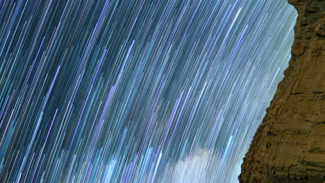 Star-trails-illuminate-the-sky-with-colorful-vertical-lines-with-the-edge-of-a-sandstone-cliff-in-the-foreground