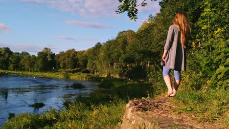 Caucasian-woman-standing-barefoot-at-the-edge-of-a-beautiful-lake-at-Bauska,-Latvia
