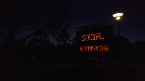 Soziales-Distanzierendes-Elektrisches-Zeichen-Nachts-Im-Park-Mit-Einer-Straßenlaterne,-Slowmo