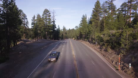 Dark-SUV-truck-drives-alone-down-a-four-lane-highway-through-a-dense-pine-forest-in-the-late-afternoon