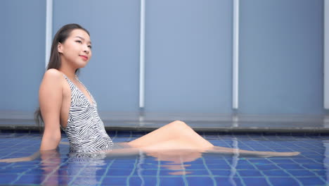 Young-petite-asian-woman-in-swimsuit-enjoying-in-water-of-hotel-swimming-pool