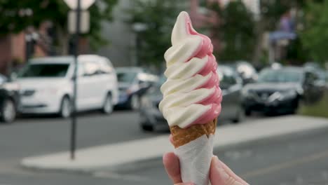 Hand-holding-a-colorful-soft-ice-cream-cone-in-the-foreground-and-turning-it-on-itself-on-a-nice-busy-summer-day