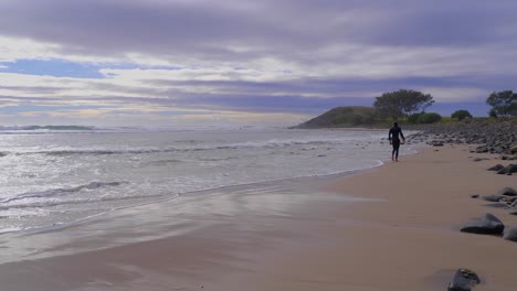 Surfer-walking-on-the-rocky-beach-of-Crescent-Head---NSW-Australia