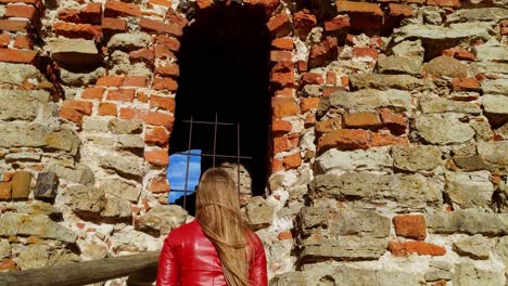 Woman-walking-up-to-a-ruined,-red-brick-doorway-at-Bauska-Castle,-Latvia