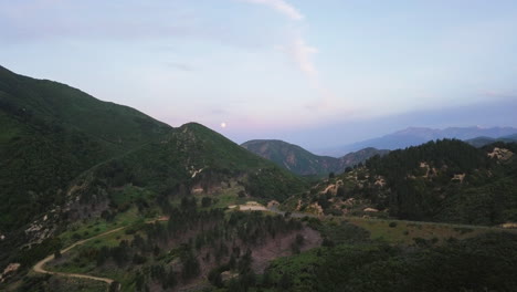 La-Luna-Se-Pone-Sobre-Una-Hermosa-Cadena-Montañosa-Verde-Salpicada-De-Pinos-Y-Atravesada-Por-Caminos