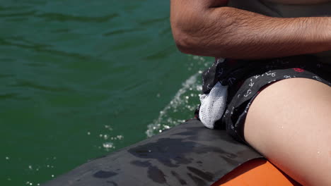 Man-Dips-Hand-Into-The-Water-While-Riding-On-A-Rubber-Boat-Speeding-Over-The-Lake-On-A-Sunny-Day---extreme-close-up