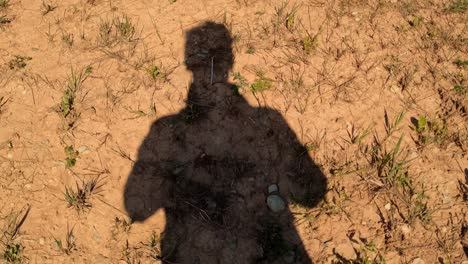 POV-of-man's-shadow-walking-on-orange-dry-land,-dolly-in,-high-angle,-day