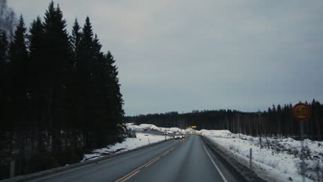 POV-car:-driving-on-rural-countryside-asphalt-highway-with-traffic-passing-by-from-Helsinki-to-Vuokatti-Finland-on-cold-winter-snow-covered-ground-on-cloudy-day-at-dusk,-handheld