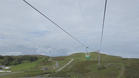 Green-cable-car-gondola-sightseeing-transportation-passing-across-scenic-mountain-valley-hillside