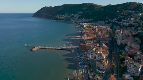 Drone-Volando-Hacia-Atrás-Desde-La-Ciudad-De-Laigueglia,-Liguria-Durante-La-Puesta-De-Sol