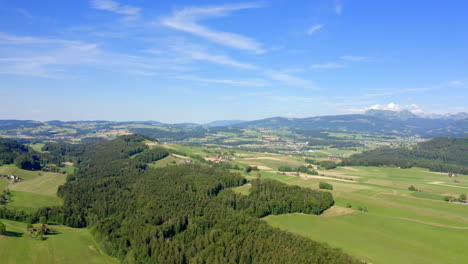 Swiss-Countryside-With-Lush-Green-Fields-And-Forest-Under-Blue-Sky-In-Vaud,-Switzerland---Aerial-Drone-Shot