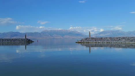 Fly-through-shot-of-the-entrance-to-Saratoga-Springs-Marina-on-Utah-Lake-from-the-end-of-a-red-pontoon-following-channel-buoys-with-distant-mountains-in-the-background-reflecting-off-the-calm-water