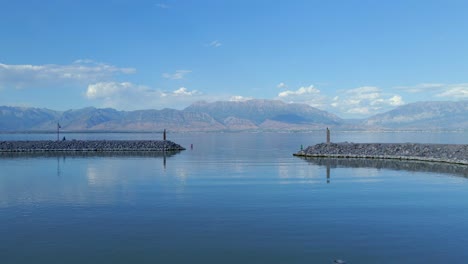 Slow-dolly-shot-of-marina-entrance-to-Saratoga-Springs-on-Utah-Lake-between-the-rocky-marina-walls-with-sunlit-mountains-in-the-background