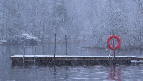 Heavy-snowfall-on-a-river-with-dock-and-lifebuoy,-tripod-shot