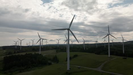 Gray-Clouds-Over-Rows-Of-Wind-Turbines-Generating-Renewable-Energy-On-The-Vast-Field-In-Quebec,-Canada-At-Dusk---aerial-drone,-pullback-shot