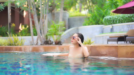 Thai-fashion-woman-leaning-at-the-edge-of-the-pool-in-a-tropical-setting