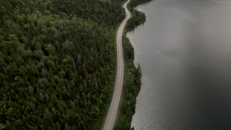 Long-And-Winding-Road-By-The-Lush-Forest-And-Calm-Lake-In-Gaspe-Peninsula,-Quebec,-Canada---aerial