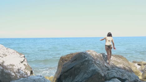 Junge-Attraktive-Frau-Im-Zweiteiligen-Bikini,-Der-über-Felsen-Nahe-Dem-Strand-Klettert