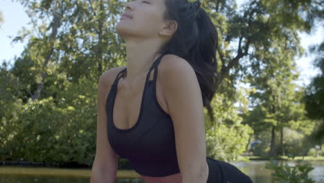 Young-woman-doing-upward-dog-yoga-pose-in-beautiful-park