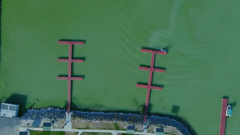 Bird's-eye-view-of-emerald-green-water-in-the-Saratoga-Marina-in-Utah-Lake-panning-upwards-with-three-red-pontoons-and-waves-rippling-across-the-marina