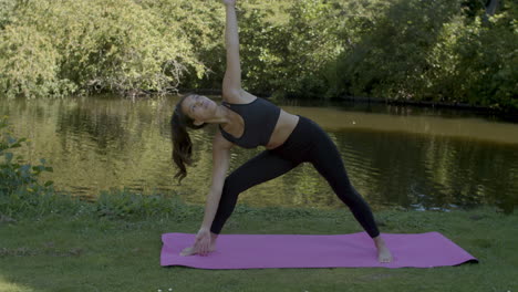 Young-woman-doing-sun-pose-yoga-exercises-near-pond