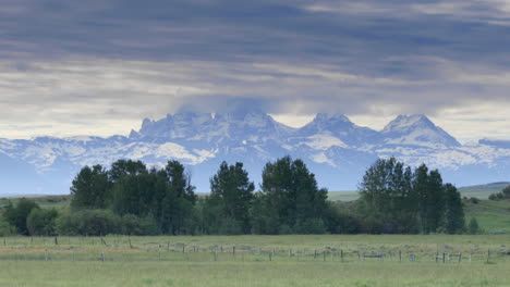 Car-drives-past-snowy-Wyoming-mountains-viewed-from-Idaho-side,-long-shot