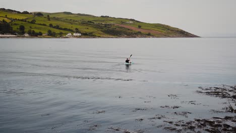 Man-kayaking-in-the-sea-with-countryside-in-background