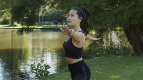 Young-woman-doing-warrior-pose-in-beautiful-green-park