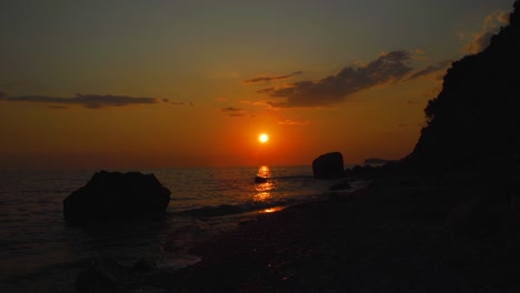 Meereslandschaft-Mit-Felsigem-Strand,-Der-Vom-Meer-Umspült-Wird-Und-Einen-Wunderschönen-Sonnenuntergang-Mit-Orangefarbenem-Bewölktem-Himmel-Widerspiegelt