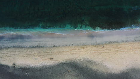 Luftaufnahmen-Von-Oben-Nach-Unten-Von-Einem-Zweifarbigen-Sandstrand-Und-Den-Sanften-Wellen-Mit-Einer-Person,-Die-Langsam-Am-Strand-Vorbeigeht