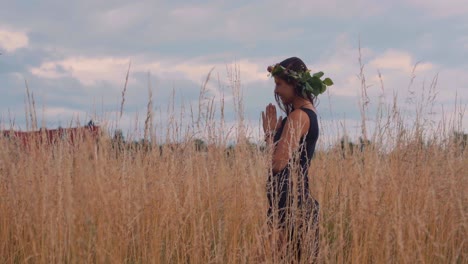 Young-Female-With-Floral-Wreath-on-Head-Praying-to-God-in-Tall-Countryside-Grass