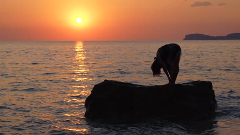 Junge-Frau-Stellt-Yoga-Meditationsübungen-über-Einer-Großen-Klippe,-Die-Bei-Schönem-Sonnenuntergang-Vom-Meer-Gewaschen-Wird