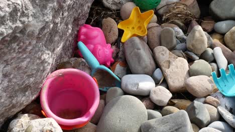 Top-down-above-stone-pebble-beach-discarded-children's-colourful-bucket-and-toys-pollution