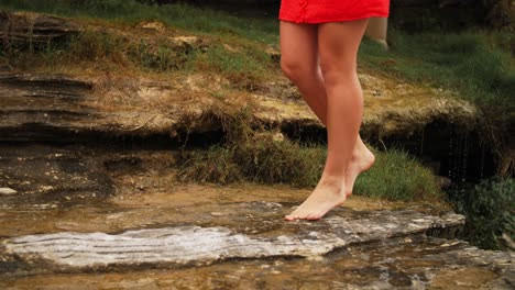 Girl-In-Red-Dress-Tiptoeing-On-The-Wet-Rocks-With-Water-Dripping-On-The-Background---Beach-In-The-Eastern-Suburbs,-New-South-Wales,-Australia
