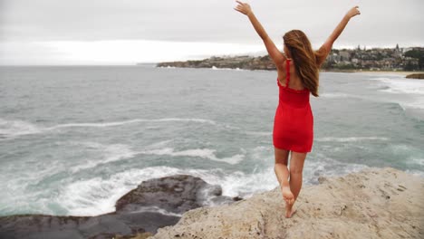 Girl-Put-Hands-In-The-Air-As-She-Watches-The-Crashing-Waves-In-The-Rocks---Eastern-Suburbs,-Sydney,-New-South-Wales,-Australia
