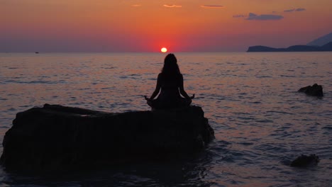 Girl-concentrated-on-Yoga-exercises-stays-frozen-on-cliff-with-sea-view-in-front-of-sunset-with-colorful-sky