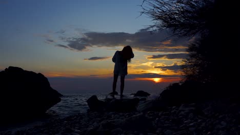 Silhouette-Eines-Mädchens,-Das-Auf-Den-Klippen-Des-Strandes-Steht-Und-Einen-Wunderschönen-Sonnenuntergang-Mit-Buntem-Bewölktem-Himmel-Beobachtet