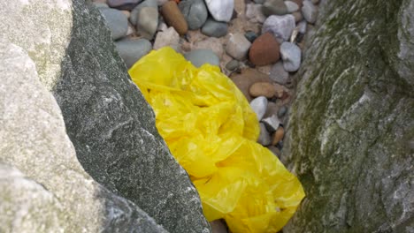 Beach-old-junk-waste-plastic-bag-between-rocky-stone-pebble-beach