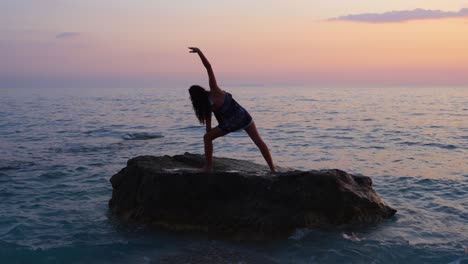 Athletenmädchen-Stellen-Yoga-Übungen-über-Einer-Klippe,-Umgeben-Von-Meerwasser-Bei-Sonnenuntergang-Mit-Glühendem-Himmel