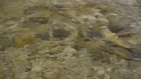 Water-flow-texture-with-riverbed-pebbles-under-crystal-cold-river,-liquid-pattern
