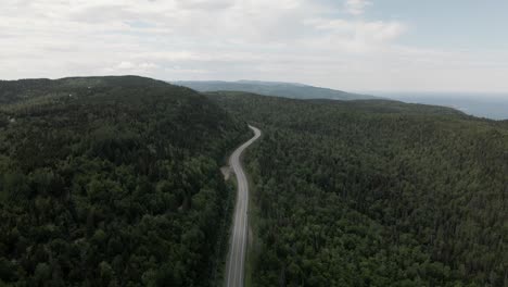 Sobrevolando-Los-Frondosos-árboles-Verdes-En-El-Bosque-Que-Rodea-La-Carretera-De-Montaña-En-Quebec,-Canadá