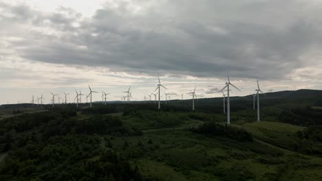 Incredible-Spinning-Wind-Turbines-Produce-Green-Renewable-Energy-above-Grass-and-Tree-covered-Hills-on-a-Cloudy-Day