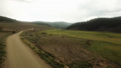 Looping---Aerial-view-of-gravel-road-running-thru-a-mountain-meadow-in-Colorado-on-a-cloudy-afternoon