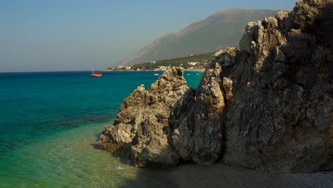 Rocky-shore-in-Ionian-sea-with-cliffs-washed-by-calm-crystal-turquoise-sea-and-boats-in-background
