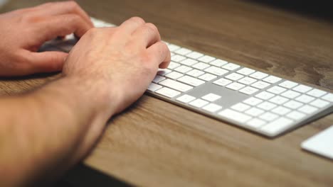Tight-panning-shot-of-hands-typing-on-a-slim-computer-keyboard-on-an-oak-desk